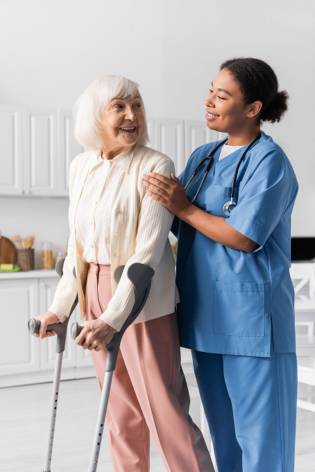 Elderly person with crutches receiving compassionate support from a healthcare professional in a home setting.